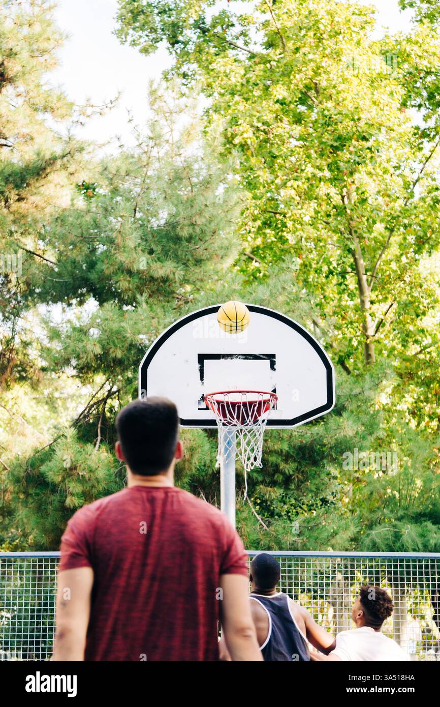 Schwarze und hispanische Männer spielen Basketball auf einem sonnigen Platz im Freien. Ein vielfältiges Teamsportimage, das sich für Fitness-, Street Basketball- und Jugendsportkampagnen eignet. Ideal für aktive Lebensstile, Teamwork und Sport-Branding. Stockfoto