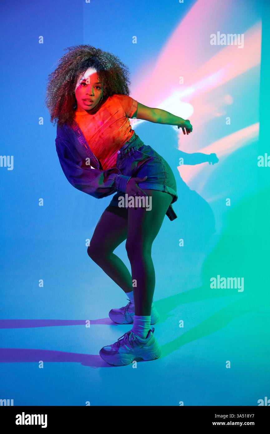 Eine schwarze Tänzerin spielt in einem Studio dynamische Routine unter Neonlichtern. Dieses energiegeladene Bild passt zu Elementen aus Tanz, urbaner Kultur und Performance. Stockfoto