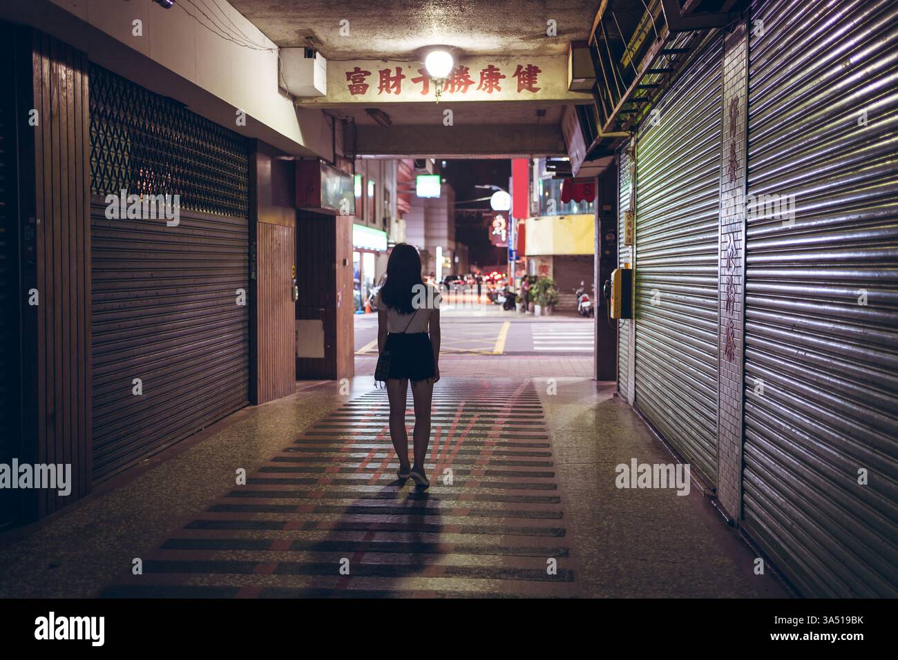 Asiatische Frau, die in einem unterirdischen Korridor steht, in einer metropolitanen Transitumgebung. Die stimmungsvolle Abenddämmerung und die urbane Kulisse machen dieses Bild ideal für Reisen, Pendelfahrten und Lifestyle-Kampagnen in der Stadt. Stockfoto