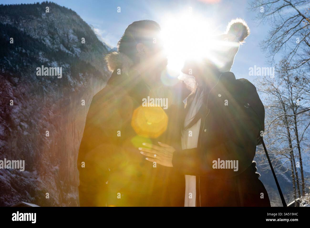 Gesichtsloses Paar umarmt sich an ihrem Verlobungstag in einer malerischen, verschneiten Bergkulisse mit strahlendem Sonnenlicht. Ein romantischer Wintermoment, ideal für Verlobungsankündigungen und alpine Reisen. Stockfoto