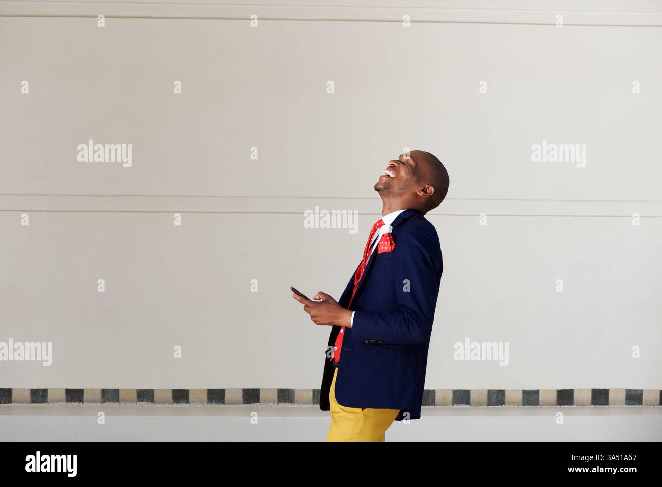 Fröhlicher afrikanischer Geschäftsmann lacht, während er auf einem Smartphone läuft und redet. Ideal für den geschäftlichen Lifestyle, mobile Technologie und urbane Erfolgsbilder. Geeignet für Startup-, Networking- oder alltägliche professionelle Kampagnen mit Kopierbereich. Stockfoto