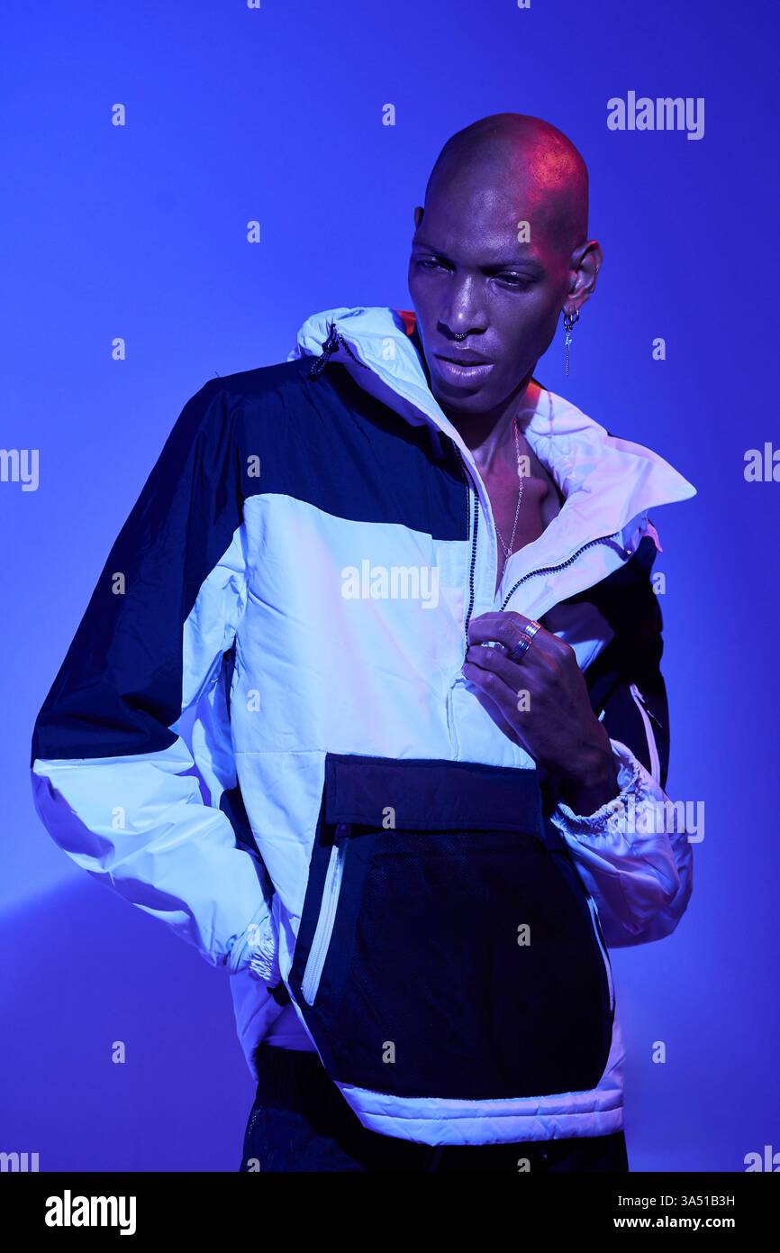 Stilvoller kahlköpfiger Mann in lässiger Kleidung posiert selbstbewusst vor blauem Studio-Hintergrund. Ein modernes Herrenporträt, das für Style- und Lifestyle-Kampagnen geeignet ist. Hervorragend geeignet für Markengrafiken mit Selbstvertrauen, moderner Herrenmode und Headshot. Stockfoto