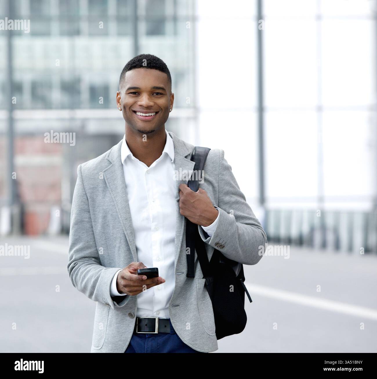 Porträt eines schicken jungen afroamerikanischen Mannes, der auf einem Handy SMS schreibt. Ein moderner Freizeitlook, der sich perfekt für Technologie- und Konnektivitätsthemen in Lifestyle- und Reisekontexten eignet. Ideal für Inhalte zu mobilen Messaging, Pendlerverkehr und alltäglicher Kommunikation. Stockfoto