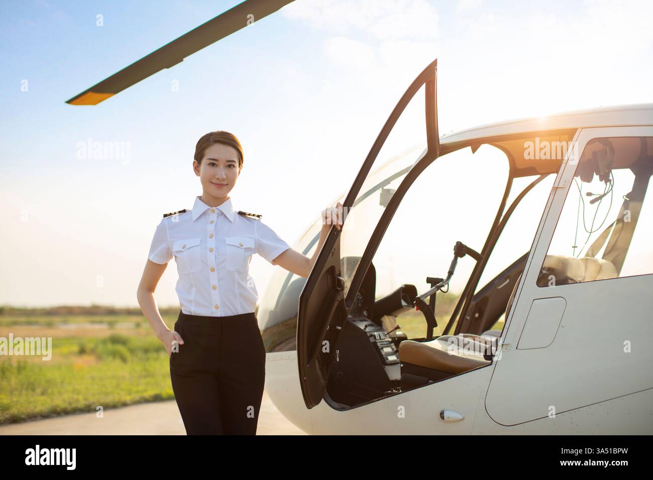 Chinesischer Hubschrauberpilot steht neben einem Hubschrauber in einer professionellen Outdoor-Umgebung. Dieses Bild zeigt Frauen in den Bereichen Luftfahrt, Luft- und Raumfahrt und MINT. Ideal für Technologie-, Transport- und Branchenkampagnen, in denen weibliche Führungsqualitäten zum Ausdruck kommen. Stockfoto
