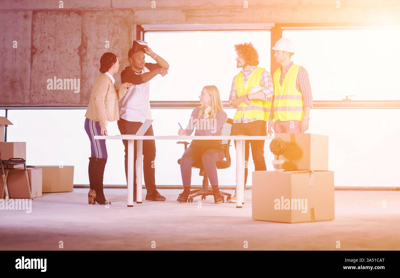 Junges multiethnisches Geschäftsteam überprüft Dokumente und Arbeitsabläufe auf einer Baustelle mit einem Virtual-Reality-Headset und Laptop. Zeigt Zusammenarbeit, Innovation und digitale Technologie in der Architektur- und Baubranche. Ideal für das Branding in Bezug auf Smart Construction, BIM, Virtual Reality und verschiedene Teams. Stockfoto