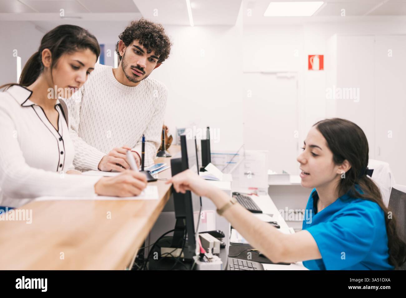Medizinisches Personal hilft einem Paar mit Papierkram an der Rezeption der Klinik. Die Szene zeigt Empfang, Check-in und Patientenbetreuung in einem modernen Gesundheitsumfeld. Ideal für das Gesundheitswesen und die Bildgebung für Verwaltungsdienste. Stockfoto