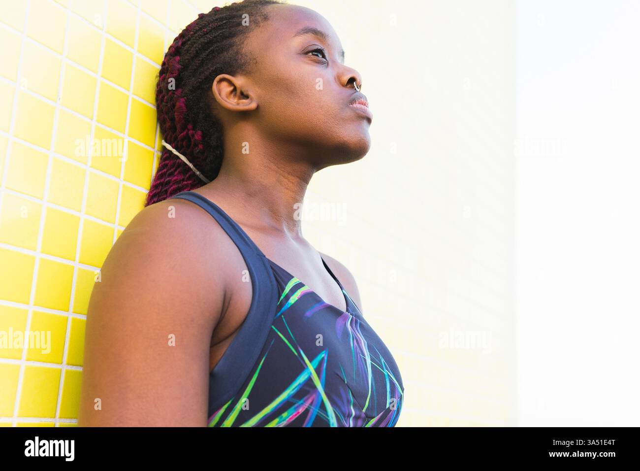 Die schwarze Athletin liegt nach dem Workout an einer gelb gekachelten Wand. Dynamische Wellness-Bilder für Fitnesskampagnen und aktive Lebensstile. Stockfoto