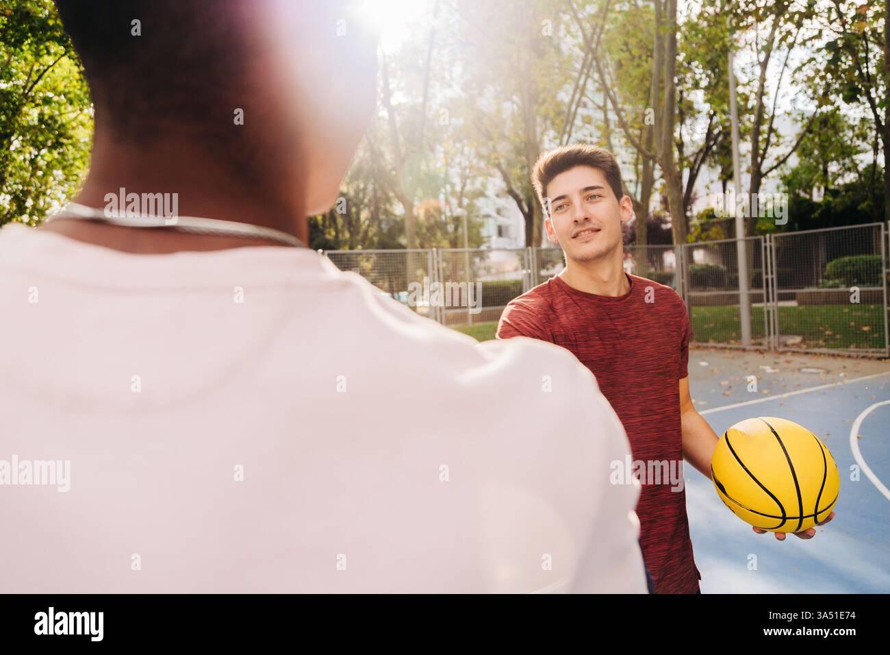 Schwarze und hispanische Männer schütteln auf einem Basketballfeld in der Nähe eines Metallzauns die Hand und halten Teamarbeit und Einheit im Sport fest. Der energiegeladene Moment passt zu Fitness, Community-Outreach und verschiedenen Branding-Kampagnen. Ideal für Sport, Jugendprogramme und kollaboratives Marketing. Stockfoto