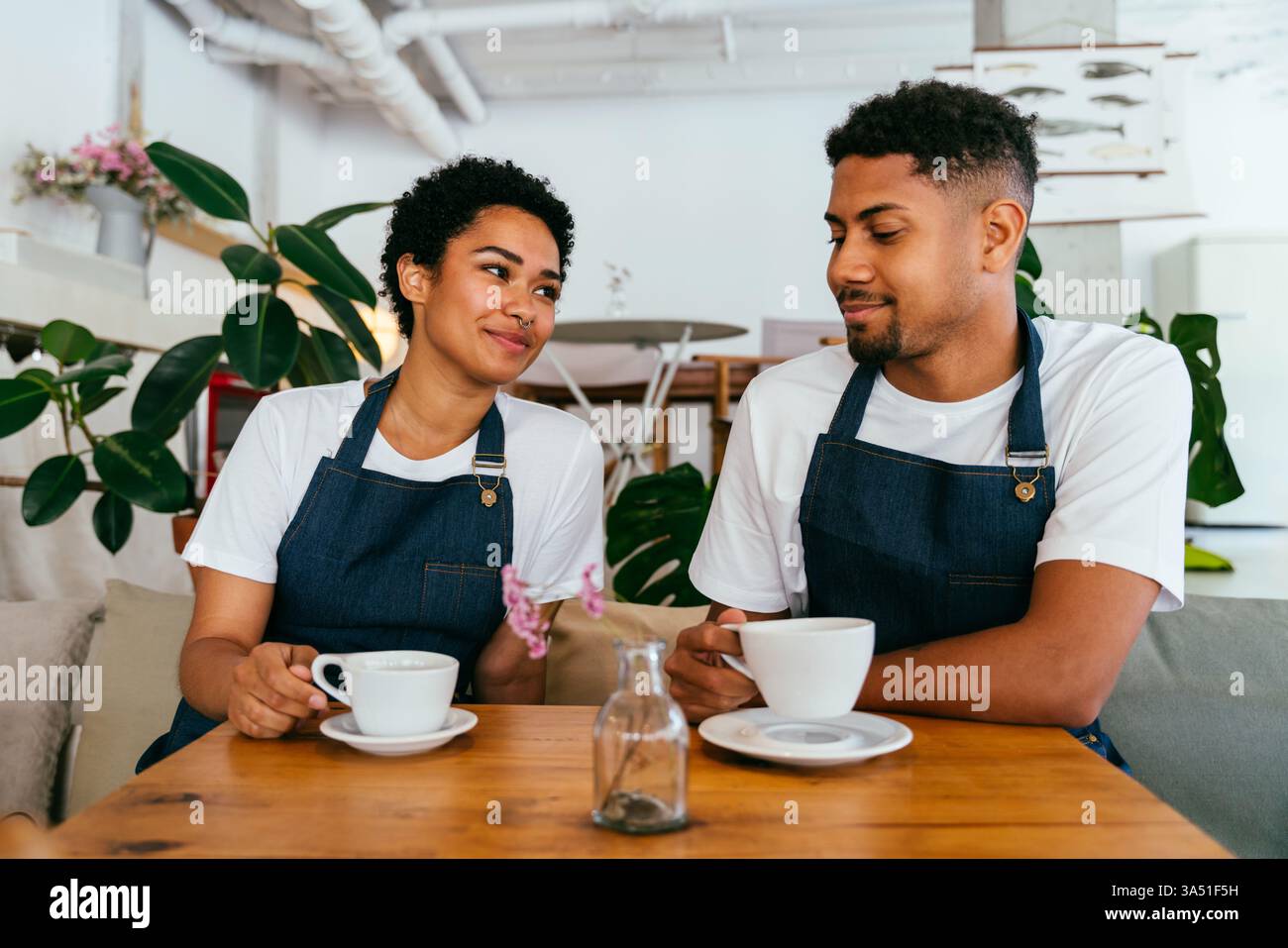 Fröhliches Porträt der Mitarbeiter im Café mit einem hispanischen Mann und einem Barista der Schwarzen Frau an einer Bäckerei. Warme, vielfältige Bilder aus dem Gastgewerbe, ideal für Coffee-Shop, Bäckerei oder Restaurantmarketing. Hebt Teamarbeit, Service und gastfreundliche Kundenerfahrungen hervor. Stockfoto