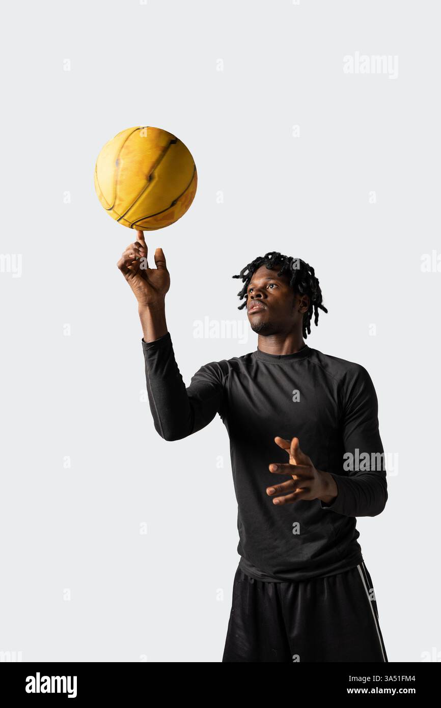 Dynamisches Bild eines afroamerikanischen Mannes in schwarzer Activewear, der Basketballtricks ausführt und während des Trainings einen gelben Ball auf seinem Finger dreht. Der neutrale graue Hintergrund betont Sportlichkeit und Können. Ideal für Sport, Fitness und Basketballtechnik. Stockfoto