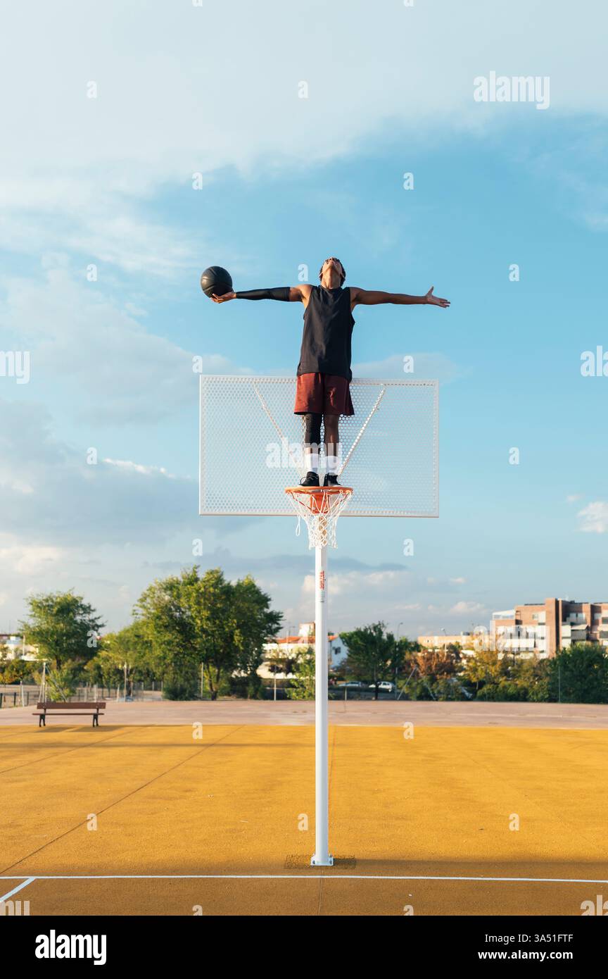 Von unten hängt ein afroamerikanischer Basketballspieler an einem Korb, der sich mit ausgestreckten Armen und einem großzügigen Kopierraum zum Himmel ausdehnt. Stockfoto