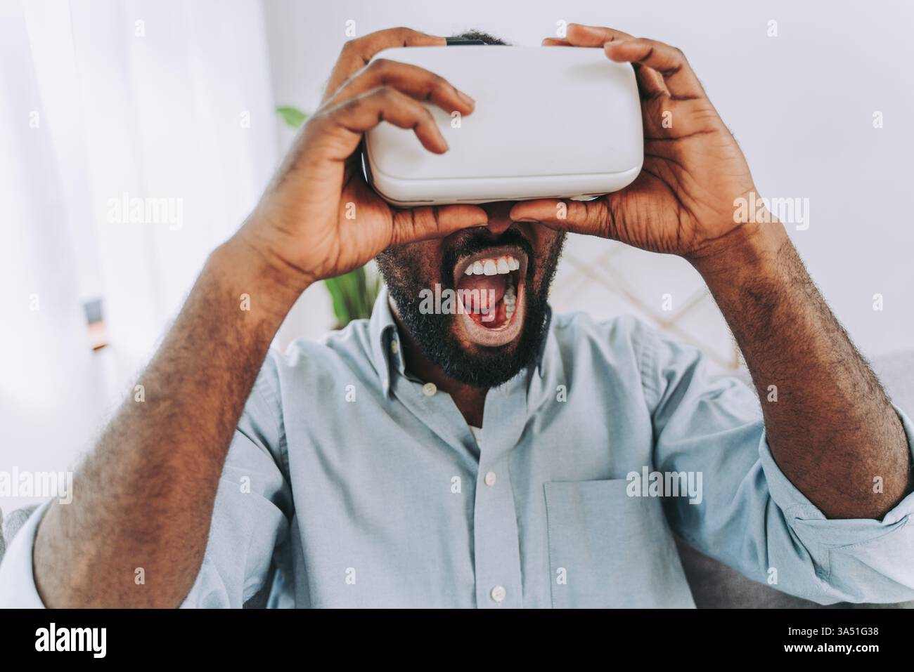 Schöner schwarzer Erwachsener zu Hause mit VR-Headset, eingetaucht in die virtuelle Realität. Ein modernes Gaming- und Technologie-Lifestyle-Bild, das sich für Home Entertainment, AR/VR-Inhalte und digitale Innovationsfunktionen eignet. Stockfoto