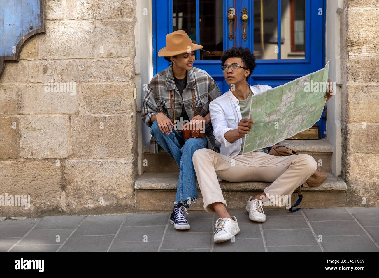 Ein junges afroamerikanisches Paar sitzt draußen vor der Tür und bespricht ihre Reiseroute. Sie planen gemeinsam Wegbeschreibungen an einem sonnigen Wochenende und halten einen Moment der Begleitung und Erkundung fest. Stockfoto
