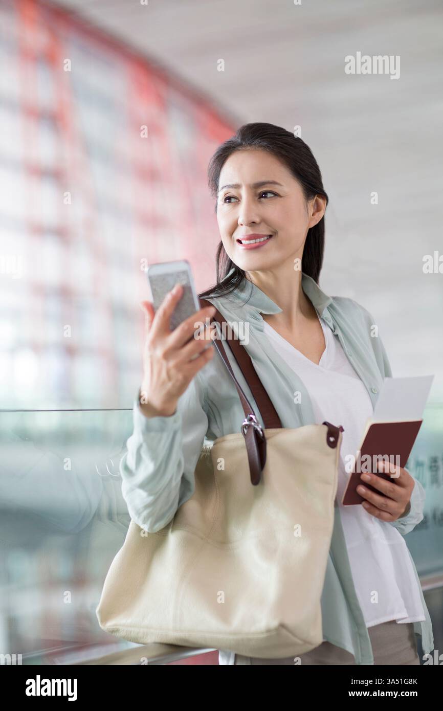 Reife Chinesin wartet am Flughafen. Casual Traveler Szene in einer Flughafenhalle mit moderner Reisetmosphäre. Nützlich für Reisen, Luftfahrt und globale Mobilität. Stockfoto