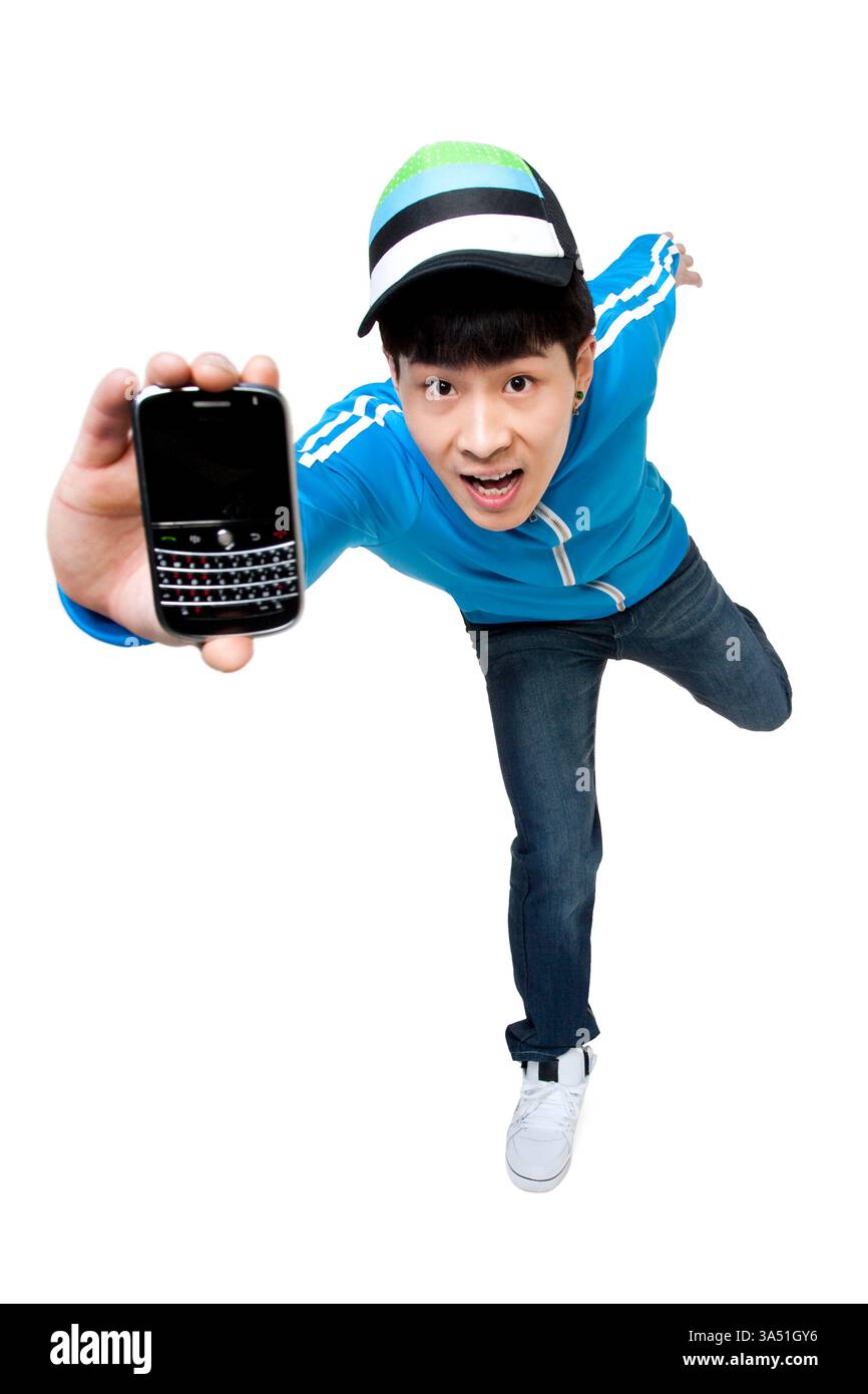 Ein chinesischer Mann balanciert auf einem Bein und hält ein Smartphone in einem Studio. Diese dynamische Pose vermittelt Energie und Jugendkultur, ideal für Technologie-, Mode- und Lifestyle-Kampagnen. Perfekt für soziale Medien, Werbung und Werbematerialien mit lebendiger Atmosphäre. Stockfoto