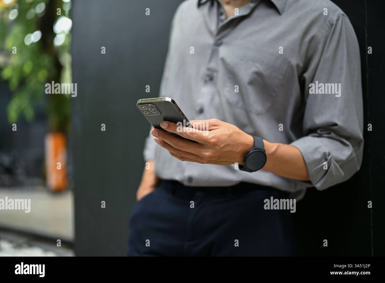 Zugeschnittenes Bild eines Geschäftsmannes, der mit einem Smartphone Nachrichten außerhalb eines Gebäudes abfragt. Saubere, moderne städtische Umgebung, die sich für Geschäftskommunikation und Mobiltechnologie eignet. Ideal für Unternehmens-, Netzwerk- und digitale Workflow-Visualisierungen. Stockfoto