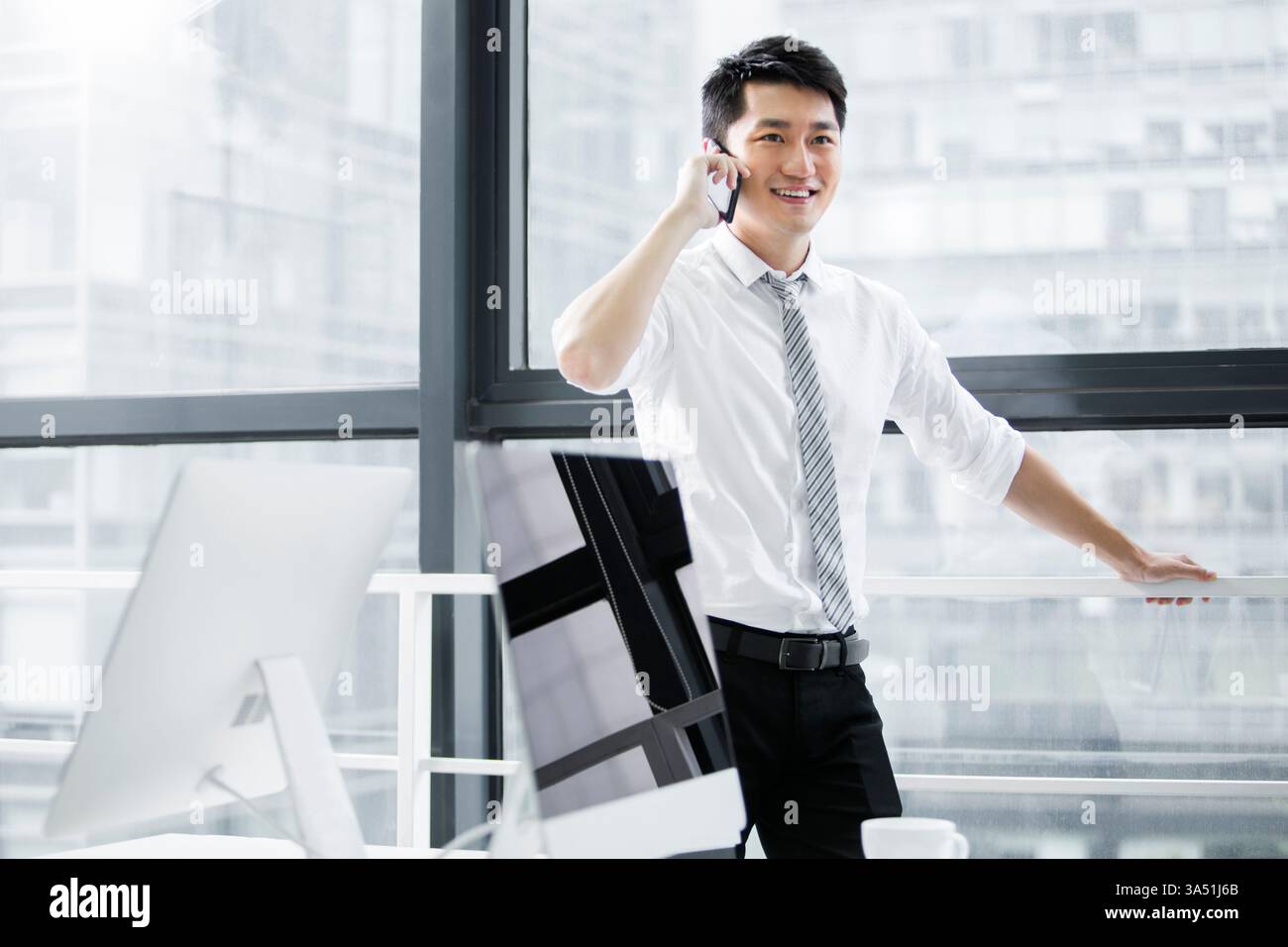 Ein chinesischer Geschäftsmann am Telefon steht in einem modernen Büro. Ideal für Unternehmenskommunikation, mobile Geschäftsabläufe und professionelle Arbeit in einem chinesischen Büro. Stockfoto