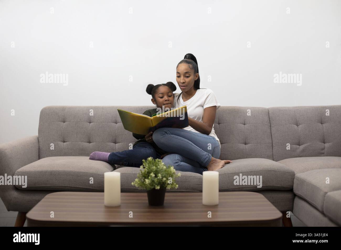 Afroamerikanische Mutter und Tochter lasen zusammen ein Buch auf der Couch und teilen sich Zeit. Ideal für Bildmaterial für Familie, Eltern und Bildung. Stockfoto