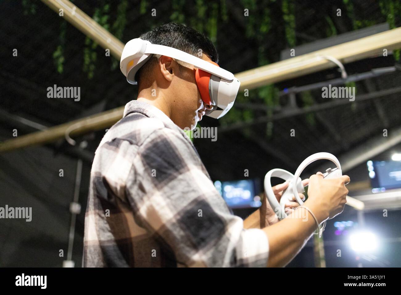 Junger Mann, der bei einem Gaming-Event mit Handheld-Controllern in eine virtuelle Realität eingetaucht ist. Ideal für Technologie, Gaming und interaktive Unterhaltungsfunktionen. Inneneinrichtung mit fokussierter, futuristischer Atmosphäre. Stockfoto