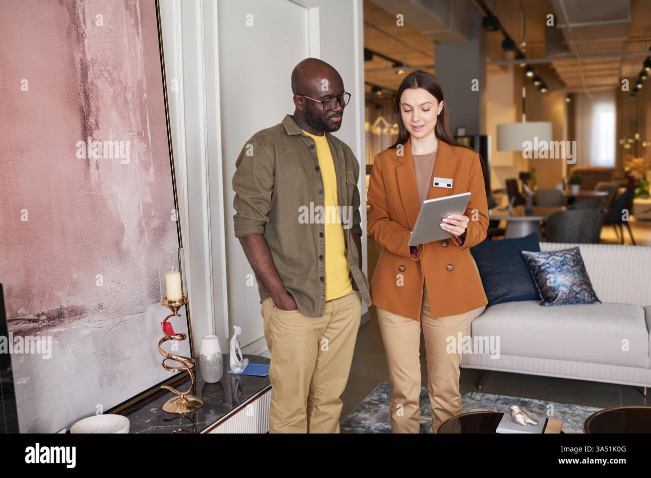 Kunde und Store Manager diskutieren neue Möbeldesigns mit einem Tablet, auf dem Produktfotos angezeigt werden. Die vielseitige Kombination steht für hilfreichen Service und das Know-how im Innenraum eines Verkaufsraums. Ideal für den Möbelhandel, die Innenarchitektur und die Visualisierung von Kundeninteraktionen. Stockfoto