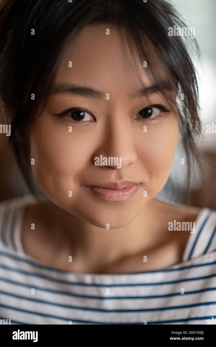 Nahporträt einer lächelnden Asiatin in 20ern Das Zuhause im Innenbereich sorgt für einen warmen, zufriedenen Ausdruck. Ideal für Lifestyle, Schönheit und visuelle Konzepte für asiatische Frauen. Stockfoto