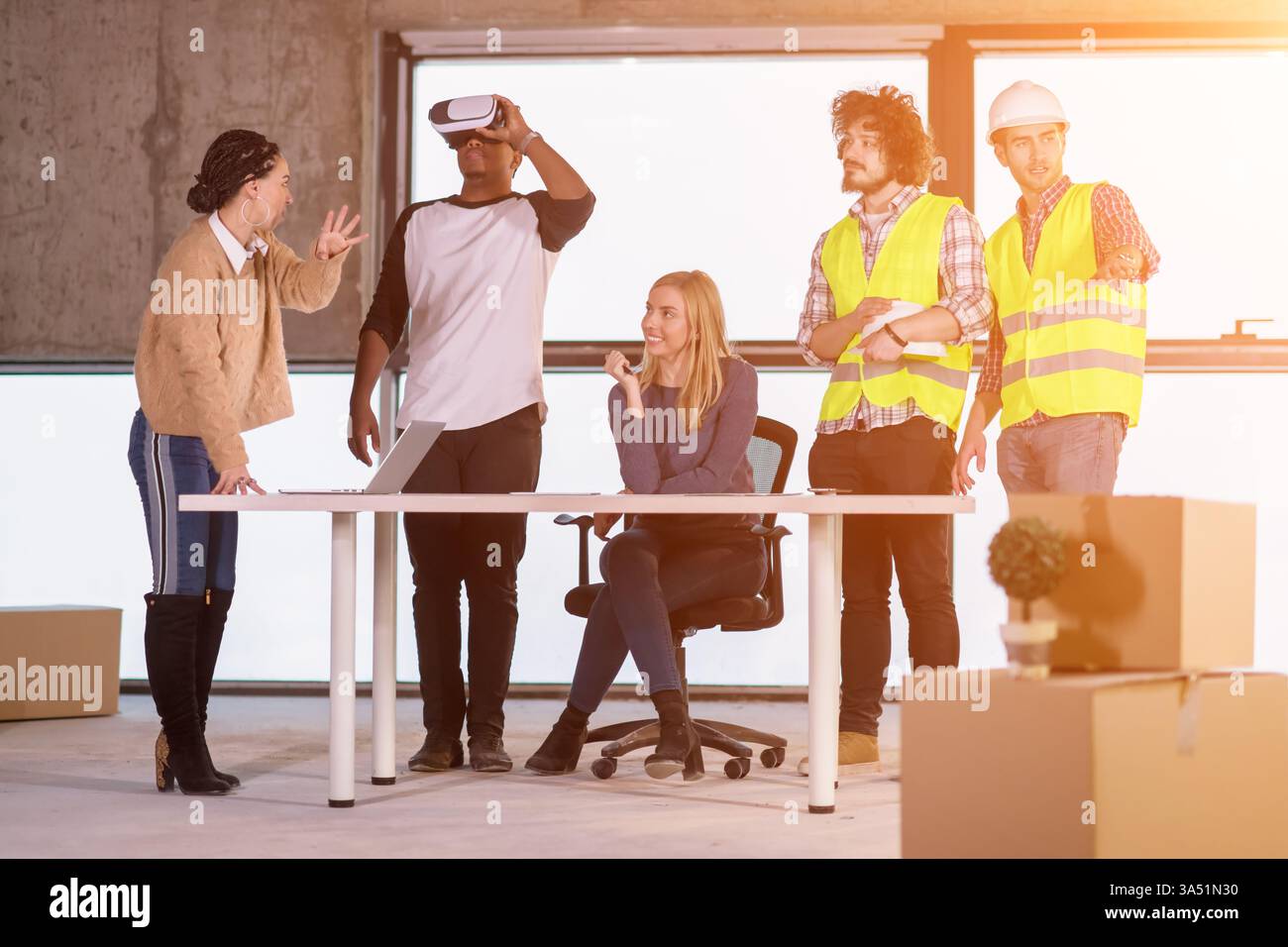 Junges multiethnisches Geschäftsteam überprüft Dokumente und Arbeitsabläufe auf einer Baustelle mit einem Virtual-Reality-Headset und Laptop. Hebt Zusammenarbeit und modernste Technologie in einem industriellen Umfeld hervor. Ideal für Kampagnen in den Bereichen Architektur, Engineering, Konstruktion und digitale Workflows. Stockfoto