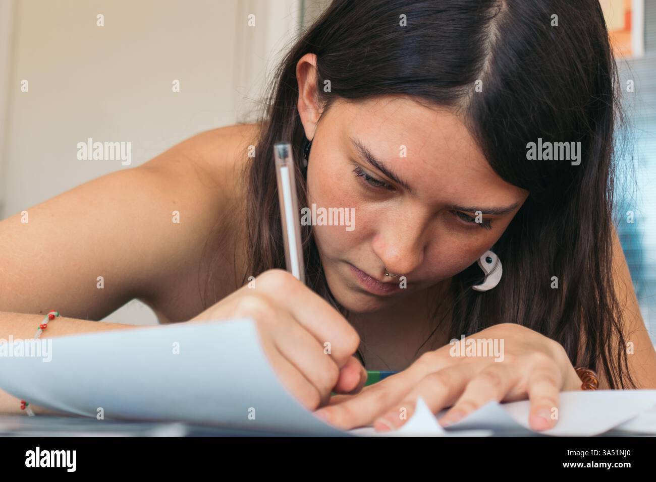 Fokussierte hispanische Tätowiererin sitzt am Tisch und zeichnet Kunst im Studio Stockfoto