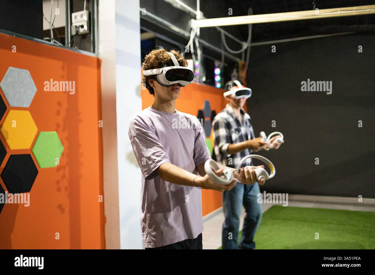 Zwei junge Erwachsene tauchten in einem angesagten Indoor-Spielbereich in ein Virtual-Reality-Spiel ein. Sie tragen VR-Headsets und halten Controller, wodurch ein mitreißendes Technikmoment entsteht. Ideal für Technologie, Unterhaltung und digitale Lifestyle-Kampagnen. Stockfoto