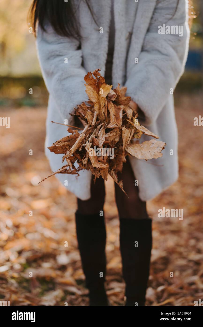 Weibliche Figur, die zwischen einem Haufen getrockneter Herbstblätter in einem Park steht. Die Herbstfarben sorgen für eine ruhige, saisonale Stimmung. Ideal für Herbst-Lifestyle, Natur und Outdoor-Visualisierungen. Stockfoto