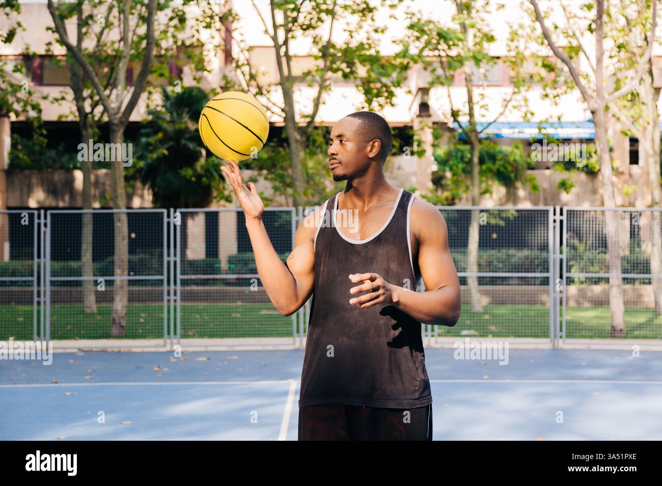 Ein schwarzer Mann, der auf einem sonnigen Sportplatz einen Basketball um den Finger dreht. Ein dynamischer Sportereignis, der Konzentration, Können und sportliches Training betont. Ideal für sportliche Motivation, Fitness-Kampagnen und Basketball-Lifestyle-Bilder. Stockfoto