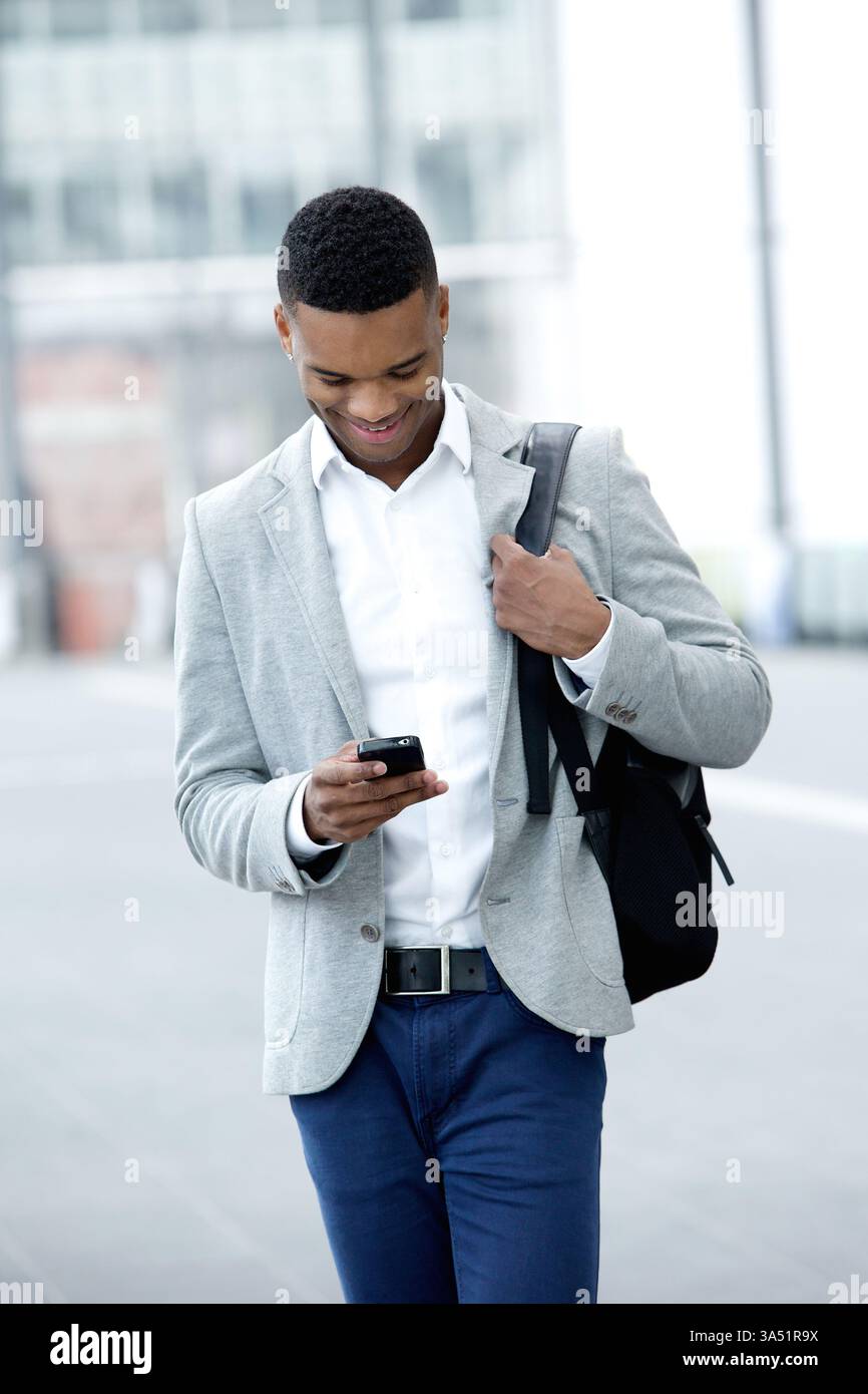 Porträt eines jungen Mannes, der auf sein Handy blickt. Ein urbanes, legeres Lifestyle-Motiv, das für Technologie- und Konnektivitätsthemen geeignet ist. Ideal für Apps, mobile Geräte und die Darstellung des täglichen Pendelverkehrs. Stockfoto