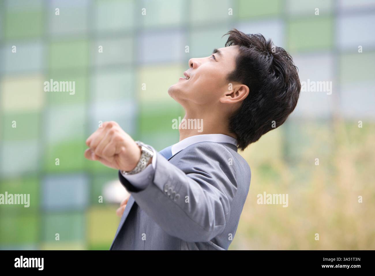 Fröhlicher chinesischer Geschäftsmann draußen vor einem Bürogebäude, der zum Feiern die Fäuste weckt. Die tagtägliche Stadtkulisse und die moderne Architektur vermitteln Leistung und Entschlossenheit. Ideal für Erfolgsgeschichten, Motivation und Geschäftswachstum. Stockfoto