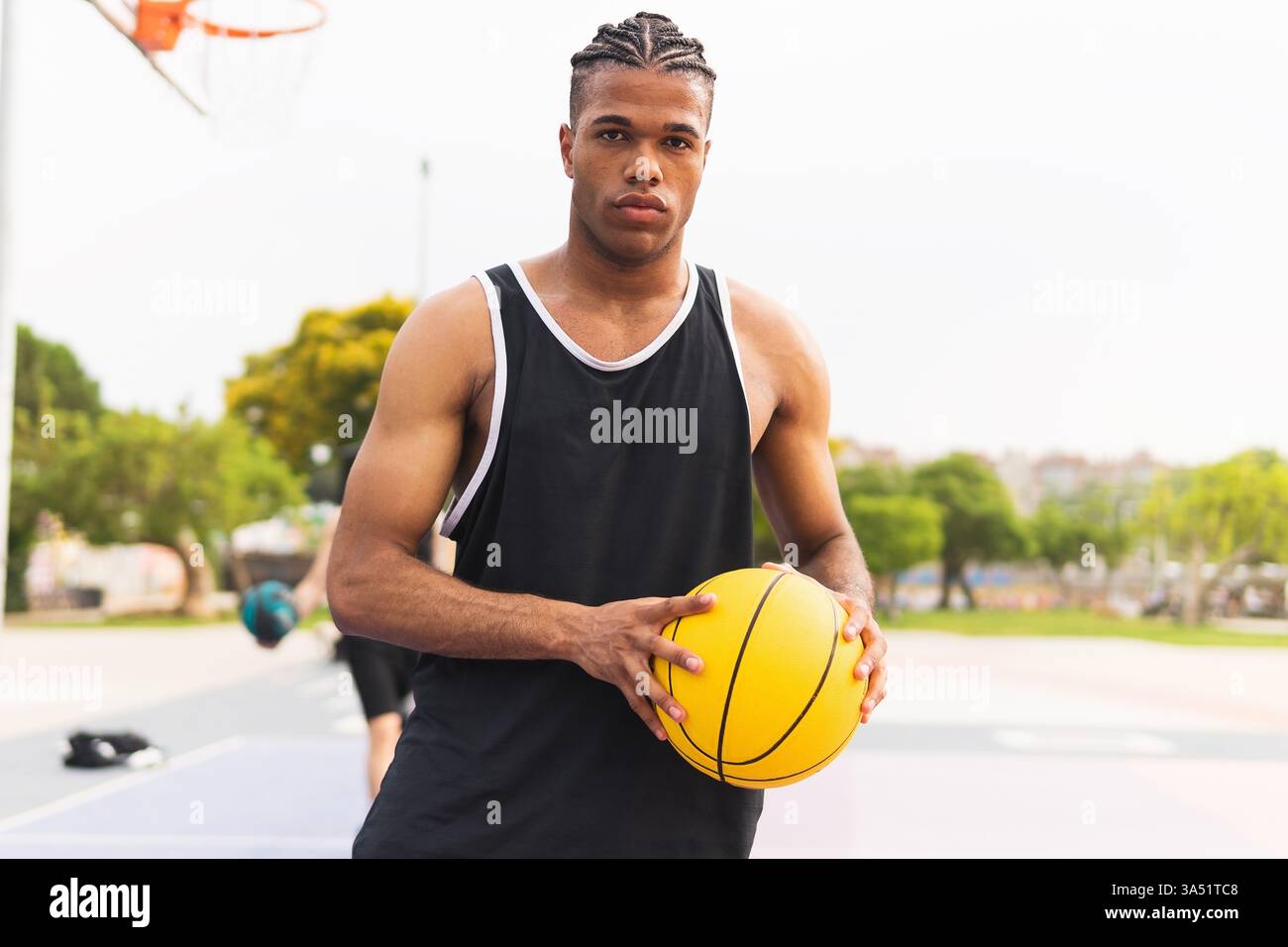 Hispanischer Mann, der einen Basketball auf einem Parkplatz hält. Er ist bereit für das Spiel und hält einen energiegeladenen Sportereignis fest. Ideal für Sport-, Fitness- und Jugendaktivitäten. Stockfoto