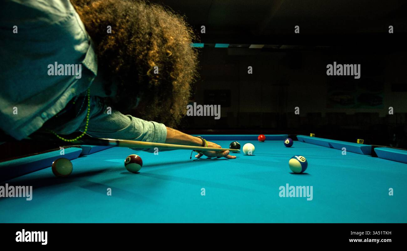 Ein hispanischer Mann in seinen 20ern will den Ball in einer Billardhalle schlagen. Ein dynamisches Sportbild, das für Billard, Billard und Spielzimmer geeignet ist. Stockfoto