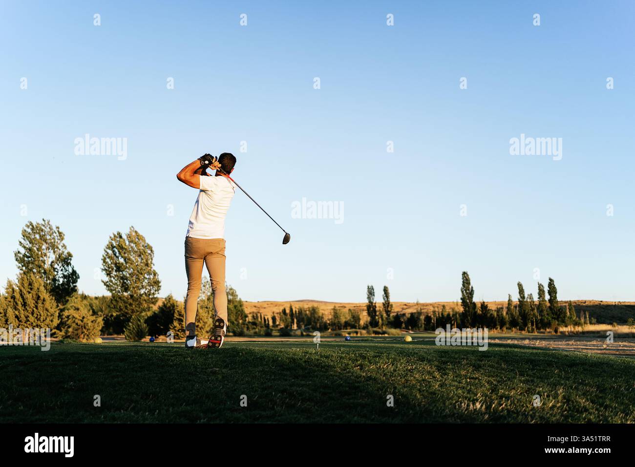 Hispanischer Golfspieler auf einem üppig grünen Golfplatz an einem sonnigen Tag, fotografiert von hinten, während er nach einem Schuss wegschaut. Ideal für Golf, Sport-Lifestyle und Outdoor-Kampagnen. Stockfoto