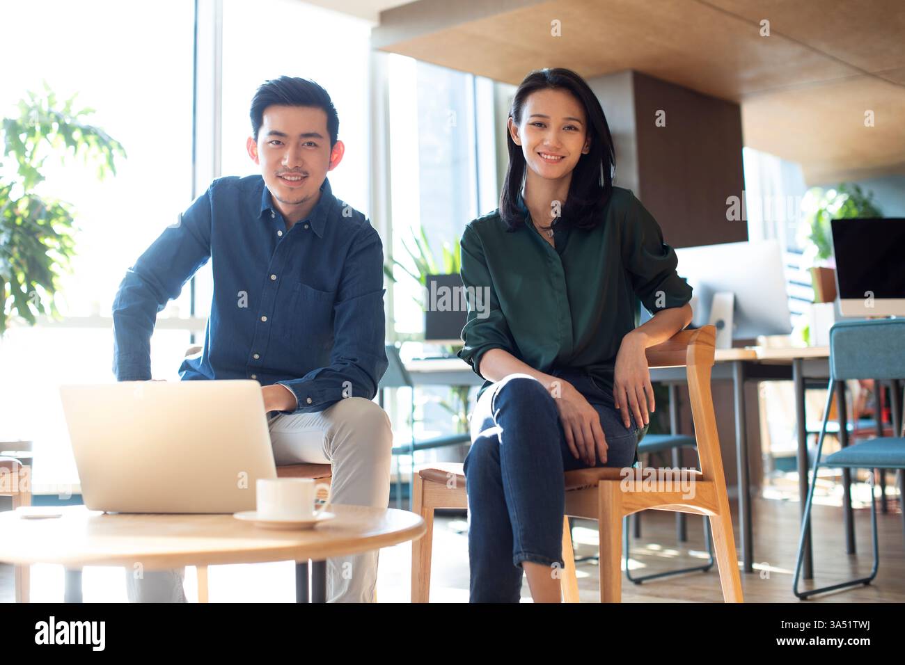 Lächelnde chinesische Geschäftsleute sitzen auf einem Stuhl mit Laptop am Tisch im Büro Stockfoto