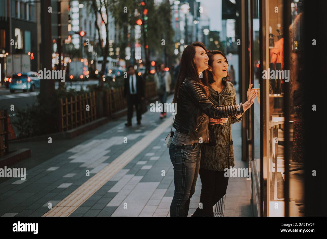 Zwei japanische Frauen, die tagsüber in Tokio einkaufen. Sie lachen und schlendern durch die Straßen der Stadt und halten Freundschaft und Stadtleben fest. Ideal für Reise-, Mode- und Shopping-Kampagnen. Stockfoto