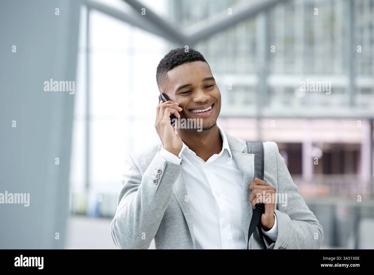 Nahaufnahme Porträt eines fröhlichen jungen Schwarzen Mannes, der lächelt, während er auf einem Handy spricht. Ideal für Lifestyle, Technologie und urbane Wohnkonzepte mit modernem, modischem Flair. Ideal für Geschichten über Pendelverkehr, Reisen und mobile Kommunikation. Stockfoto