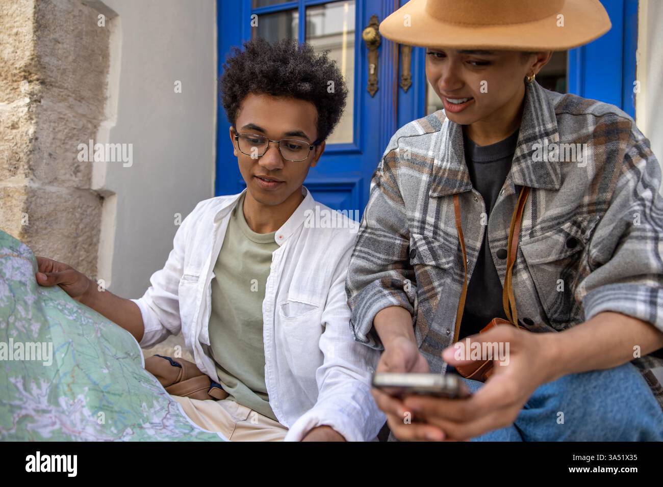 Junge afroamerikanische Paare im Freien, die eine Karte studieren, um ihre Route zu planen. Ideal für Reisen, Urlaub und Wochenendausflüge mit Entdeckungen und Zweisamkeit. Die Szene vermittelt Glück und einen aktiven Lebensstil im Sommer. Stockfoto