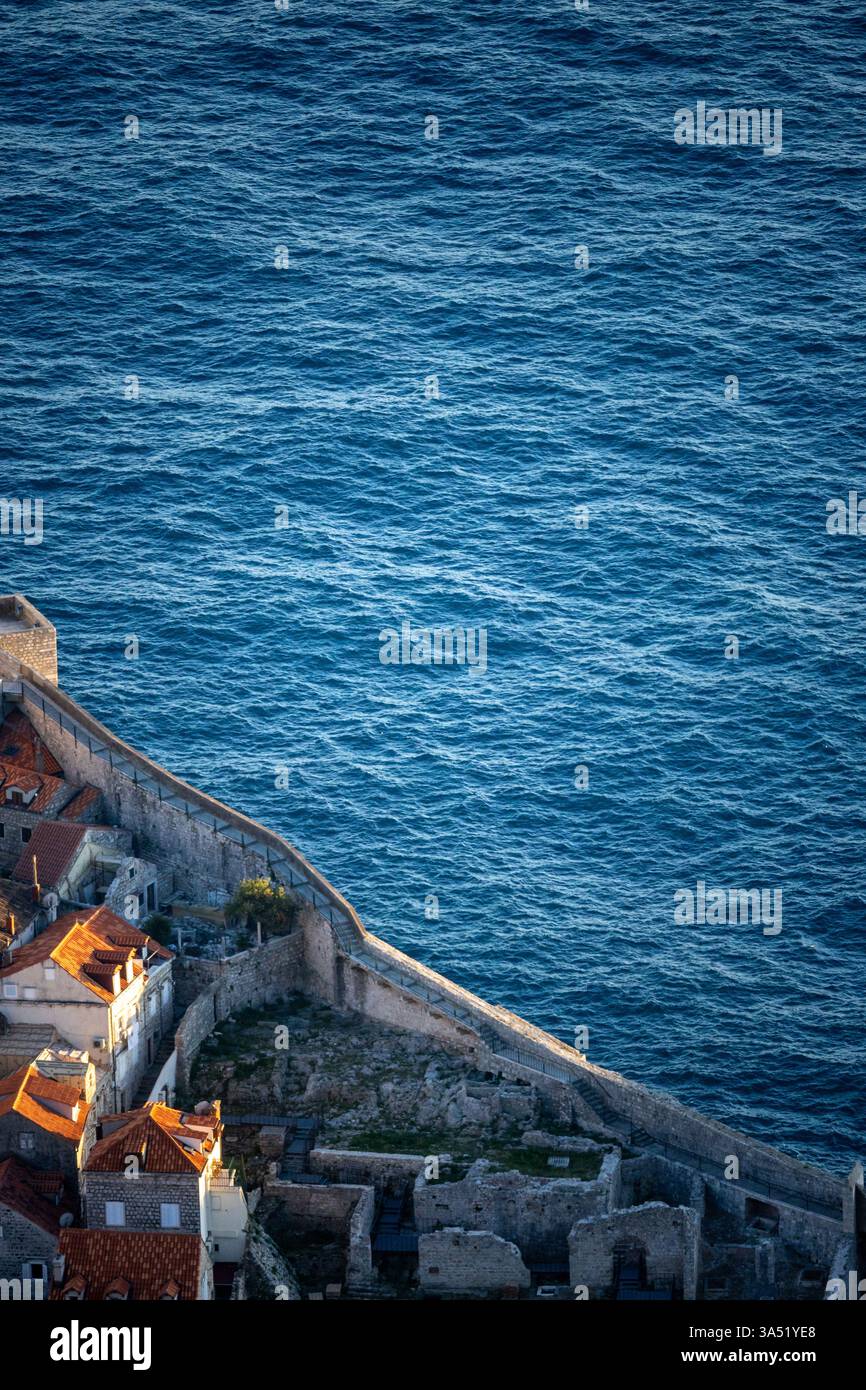 Dubrovnik, Kroatien - 01. April 2023: Stadtmauer der Altstadt von Dubrovnik, die Ruinen und das Azure Meer trennt – Tele-Hochwinkelblick im Abendlicht, vertikal Stockfoto
