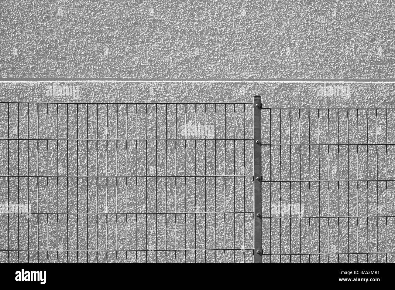 Das Detail eines homogenen Gitterzauns vor einer verputzten hellen Fassade Stockfoto