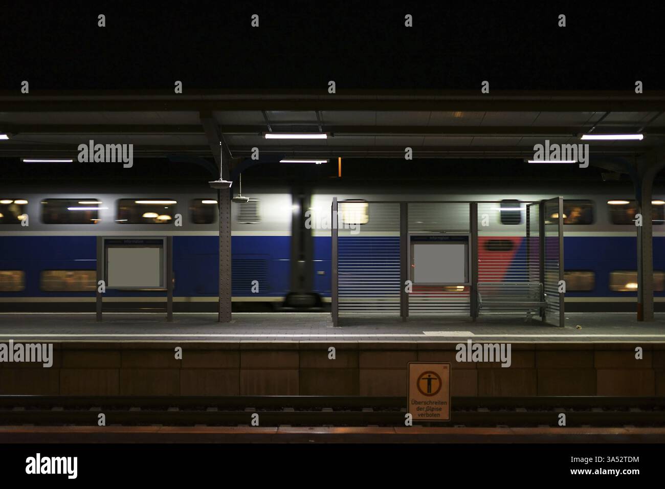 Der Bahnsteig des Bahnhofs Weinheim bei Nacht Sitzplatz an einer Glaswand und einem vorbeifahrenden Zug Stockfoto