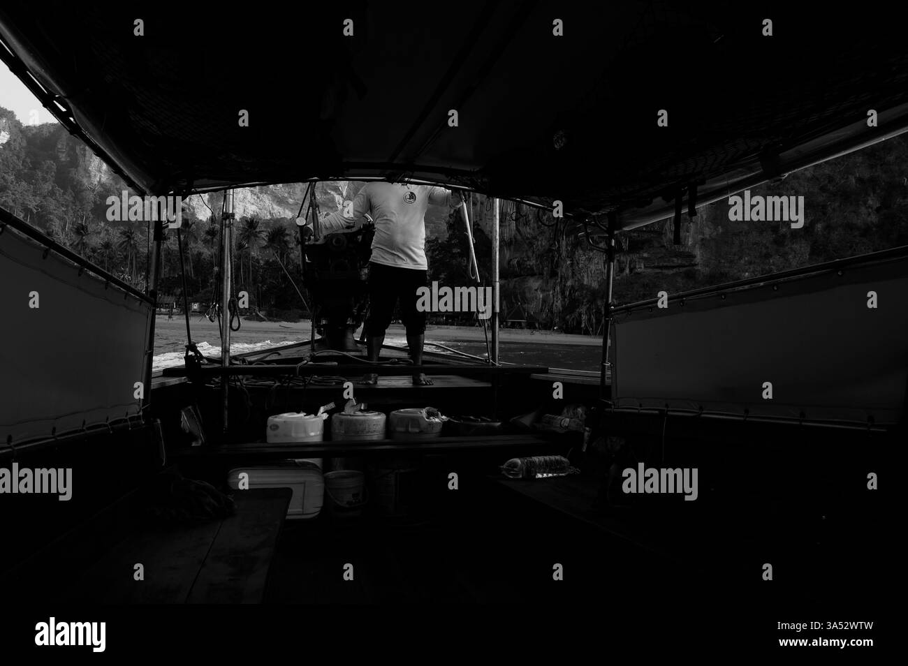 Monochrom eines Bootsmannes, der ein Langboot steuert, während er zwischen tropischen Stränden navigiert Stockfoto