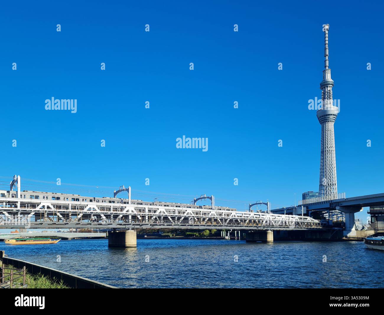 Blick auf den Sumida River mit Tokyo Skytree und Sumida River Walk in Asakusa, Tokio, mit einem Zug, der den Bergrücken überquert. Stockfoto