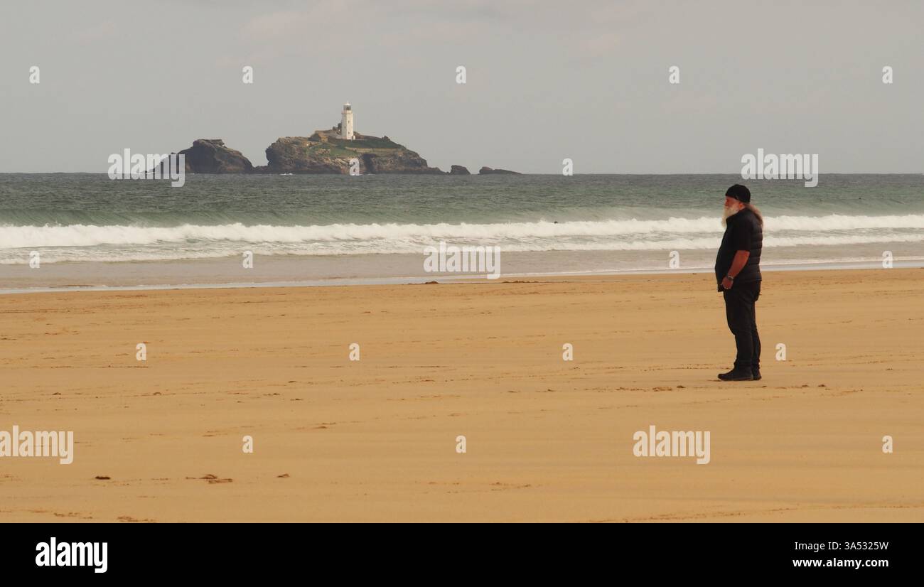 Ein bärtiger Mann am Hayle Beach mit Godrevy Point Leuchtturm und Insel im Hintergrund, Corwall, England, Großbritannien Stockfoto