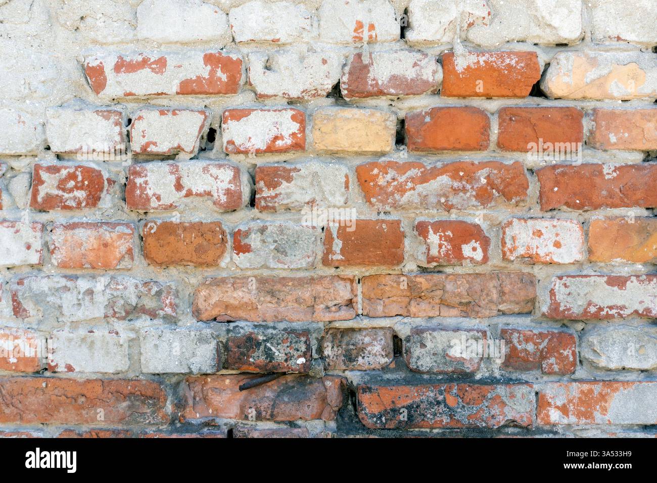 Die strukturierte Wand besteht aus einer Kombination aus roten, cremefarbenen und grauen Ziegeln, die jahrelange Witterungseinflüsse in einer städtischen Umgebung unter natürlichem Licht reflektieren. Stockfoto