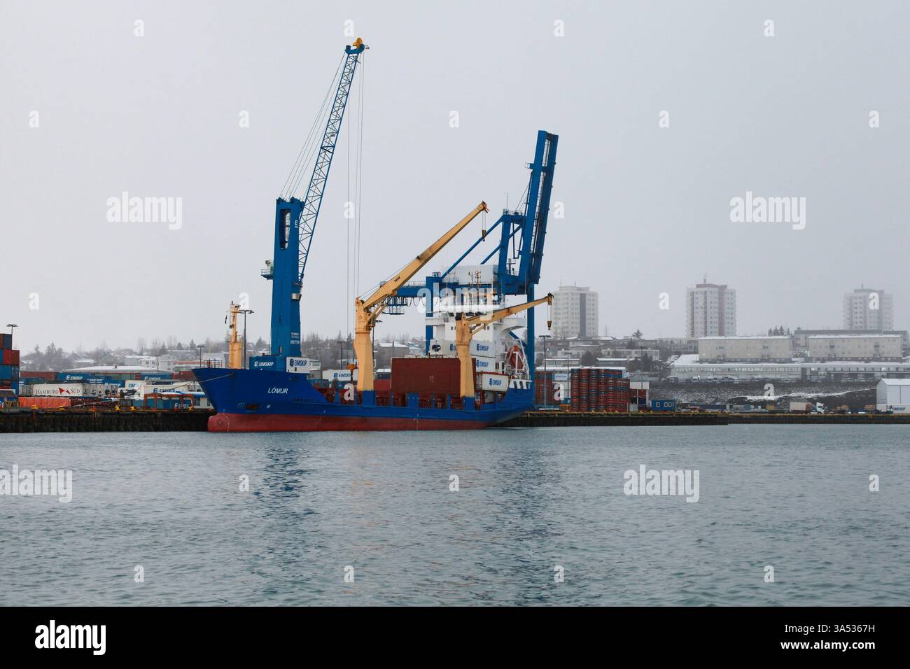 Reykjavik, Island - 4. April 2017: Ein Frachtschiff, das an einem Industriehafen mit einem entfernten Stadtbild unter einem bewölkten Himmel angedockt wurde Stockfoto