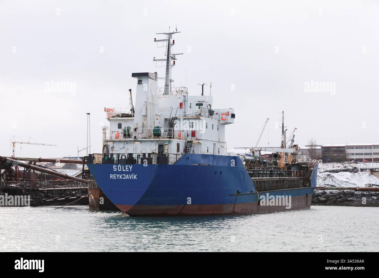 Reykjavik, Island - 4. April 2017: Ein großes blaues Frachtschiff vor Anker im Hafen von Reykjavik, umgeben von Industriebauten und Winterlandschaften Stockfoto