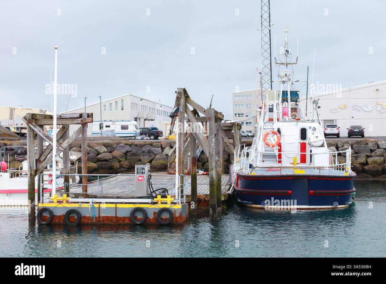 VHafnarfjordur, Island - 4. April 2017: Eine Jachthafenszene, die ein mit maritimer Ausrüstung, vertäuten Booten und Fahrzeugen ausgestattetes Dock zeigt, das gegen ein ov gestellt wird Stockfoto