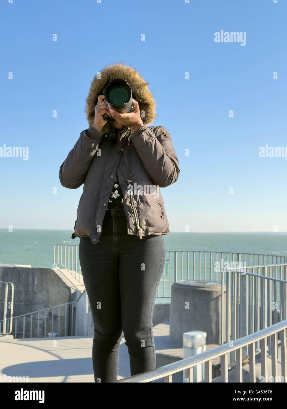 Portsmouth England Großbritannien. 18.03.2025. Frau in einer Kapuze mit Pelz im Winter, die Fotos mit einer teuren Kamera und einem Objektiv macht. Stockfoto